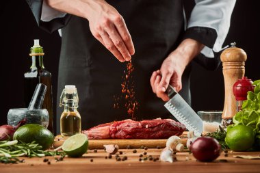 Adam etin üstüne kırmızı biber serpiyor. Çiğ biftek.