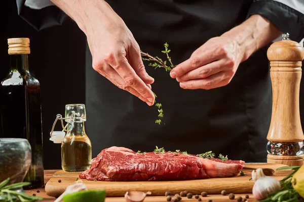 Szef kuchni rzuca liście tymianku na mięso. Profesjonalne przyprawy gotować stek wołowy — Zdjęcie stockowe