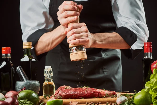 Homme utilisant un moulin à poivre pour assaisonner un steak de bœuf cru avant de griller — Photo