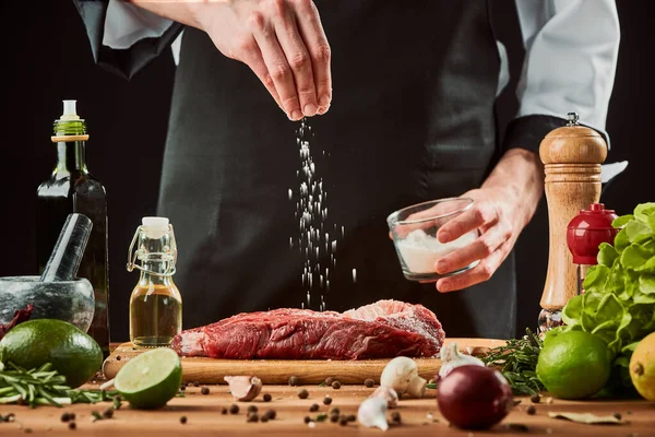 De mens strooit zout over vlees. Chef kookt een biefstuk. — Stockfoto