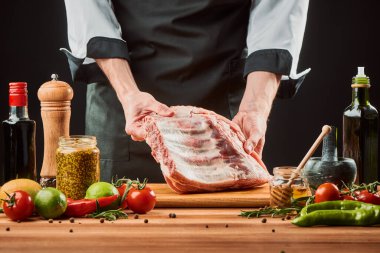 Şef ahşap kesim tahtasının üzerinde çiğ et tutuyor.