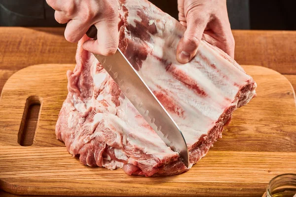 Homem cortando costelas de carne crua em uma placa de madeira — Fotografia de Stock