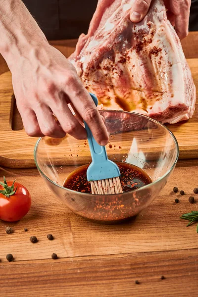 Homem mergulha escova em molho para marinar costelas de carne — Fotografia de Stock