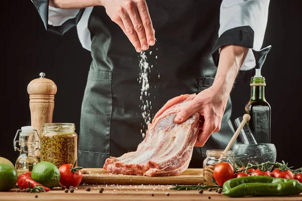 Chef zout rauwe rundvlees ribben, gooien een grote snufje op het stuk vlees — Stockfoto