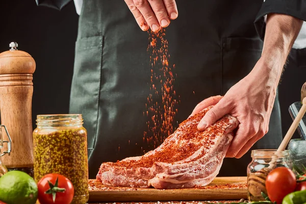 Man gooit een snufje gemalen chili op een stuk rauw rundvlees — Stockfoto