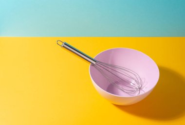 Parlak arka planda metal çırpıcı ile boş pembe kase