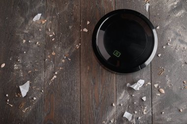 Kirli bir ağaçlıkta hareket eden siyah bir robotik elektrik süpürgesinin üst görüntüsü