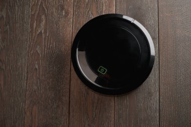 Tahta zeminde siyah bir robotik elektrik süpürgesinin üst görüntüsü