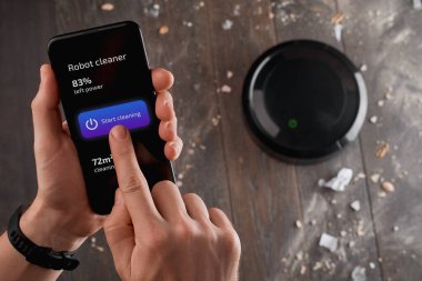 Telefonundaki uygulamayı kullanarak robot süpürgeyi çalıştıran adam.