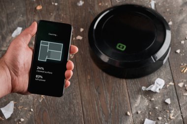 Adam telefonundaki uygulamayı kullanarak robot elektrik süpürgesini kontrol ediyor.