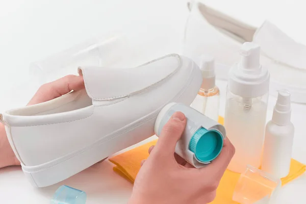 Hands polishing a white leather shoe with a sponge.