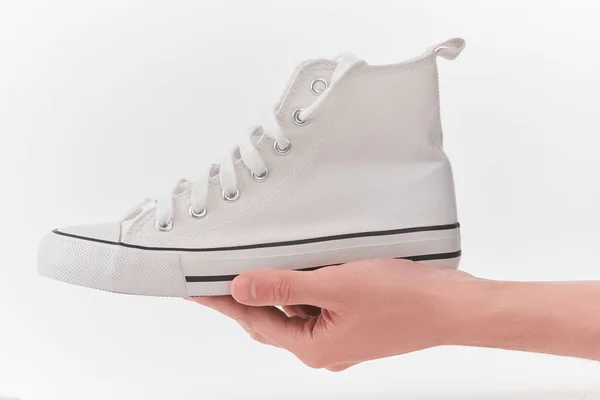 Beyaz arka planda beyaz bir spor ayakkabısı tutan el. — Stok fotoğraf