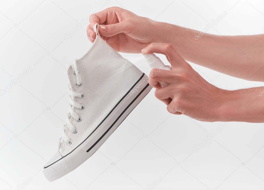 Hands holding a white canvas sneaker and spraying antiseptic