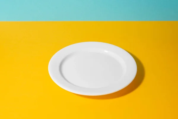 Primer plano sobre un plato blanco vacío sobre fondo amarillo y azul —  Fotos de Stock