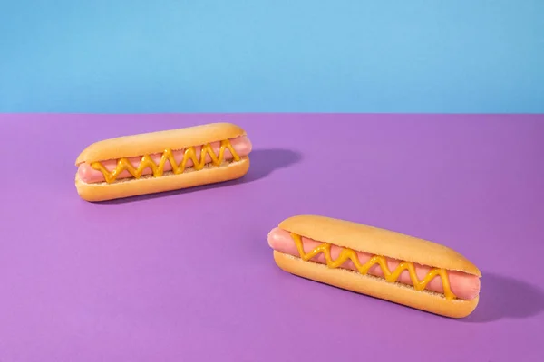 Dois deliciosos cachorros-quentes com mostarda em fundo violeta e azul — Fotografia de Stock