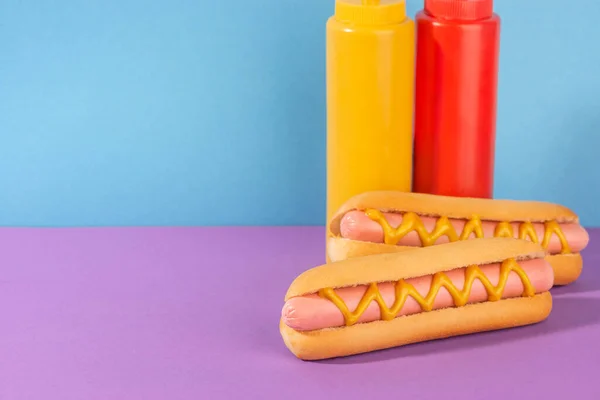 Cachorros-quentes apetitosos e garrafas de mostarda e ketchup — Fotografia de Stock