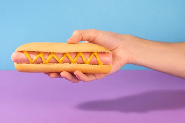 Mão dando um cachorro quente fresco com ziguezague de mostarda — Fotografia de Stock
