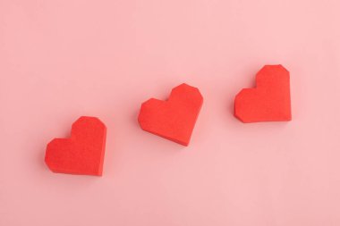 Pembe arka planda üç kırmızı kağıt kalp.