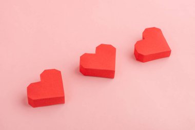 Pembe arka planda üç kırmızı kağıt kalp.