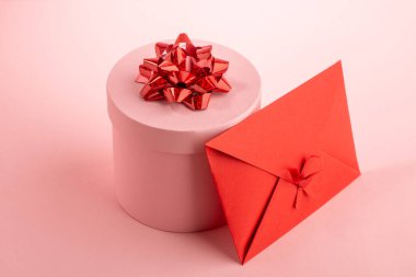 Pembe yuvarlak hediye kutusu ve pembe arka planda kırmızı zarf.