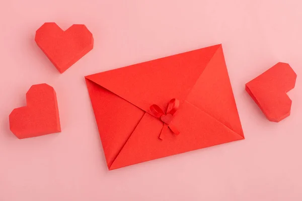 Rode papieren hartjes en enveloppe op roze achtergrond — Stockfoto