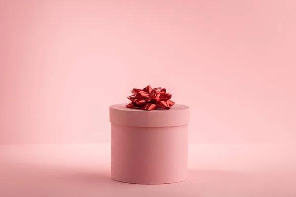Kerek ajándék doboz piros íj rózsaszín háttér — Stock Fotó