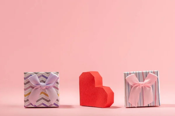 Дві подарункові коробки та червоне паперове серце на рожевому фоні — стокове фото