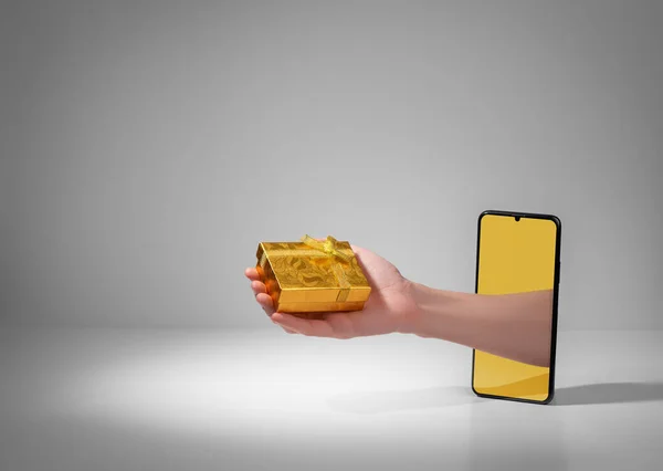 Рука дає красиву золоту подарункову коробку з екрану телефону — стокове фото