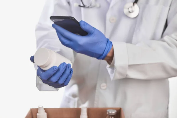 Doctor holding a bottle of pills and checking the barcode with a phone
