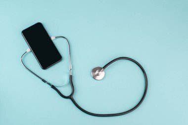 Mavi arka planda steteskobu olan bir telefonun üst görüntüsü