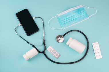 Mavi arka planda steteskobu olan bir cep telefonunun üst görüntüsü