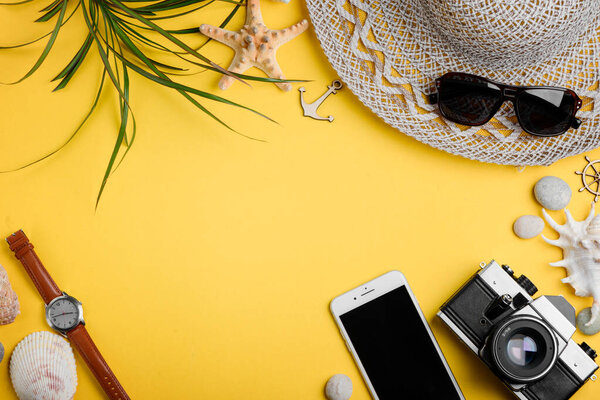 Beach accessories, phone and camera on yellow background
