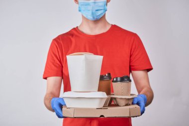 Teslimatçı elinde bir kutu pizza, tava ve kahve tutuyor.