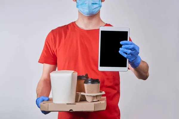 Delivery man showing a tablet with app and holding a pile of boxes with food