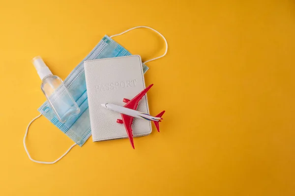 Sanitizer spray, face mask, plane toy and passport on yellow background