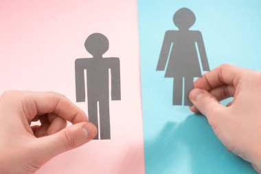 Pembe ve mavi arka planda kadın ve erkeğin kağıt bebeklerini tutan eller.