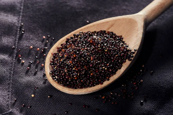 Wooden spoon with quinoa on dark napkin background — Stock Photo, Image