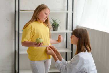 Şişman kızların belini ölçen beslenme uzmanı. Çocukluk obezitesi ve kilo kaybı