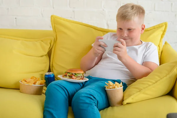 Boy playing a video game on a mobile phone with fast food