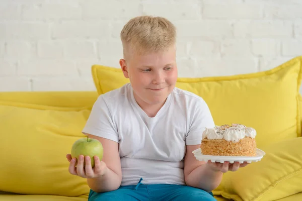 Dikke jongen die kiest tussen een appel en een taart — Stockfoto