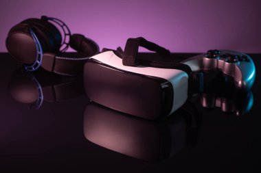 Koyu mor arka planda VR kulaklık, joystick ve kulaklık.