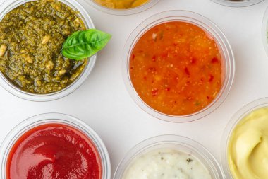 Beyaz arkaplanda küçük bardaklarda çeşitli soslar üzerine üst görünüm