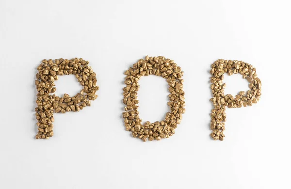 Visão superior sobre POP lettering feito de pepitas douradas no fundo branco — Fotografia de Stock