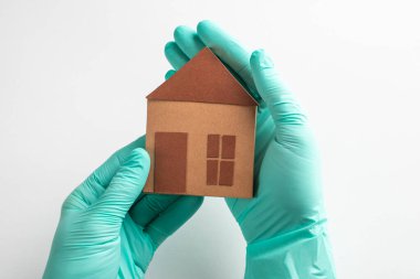 Eldivenli eller beyaz arka planda bir kağıt ev tutuyor.