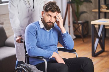 Yakışıklı sakallı adam tekerlekli sandalyede oturuyor ve doktor itiyor.