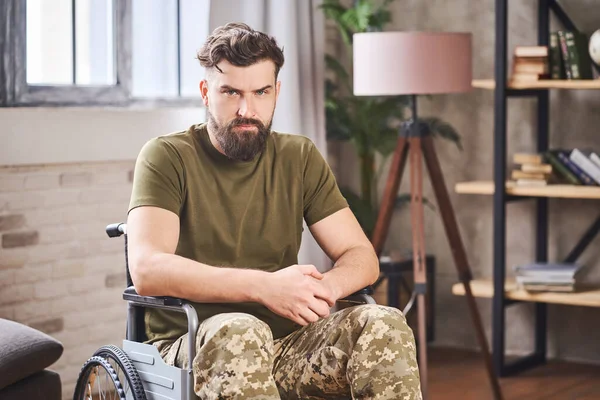 Veterano discapacitado sentado en una silla de ruedas y dando una mirada triste a la cámara —  Fotos de Stock