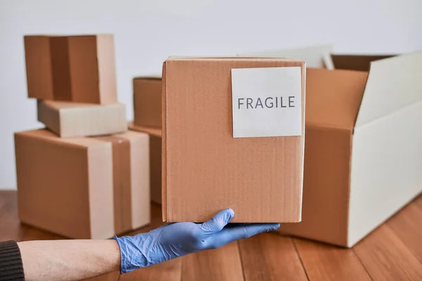 Hand in glove holding a cardboard box with fragile label — Stock Photo, Image