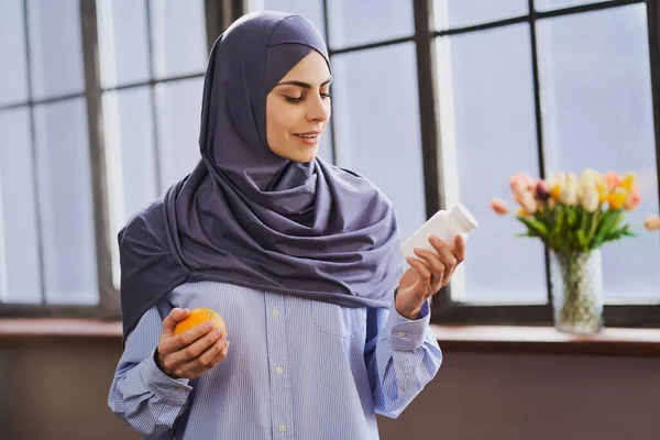 Arabian female health blogger holding an orange and a bottle of pills