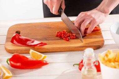 Ahşap bir tahtada kırmızı biberi küçük zarlara kesen bir adam.