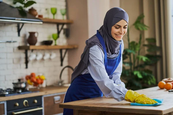 Mujer musulmana alegre limpiando una mesa en la cocina —  Fotos de Stock